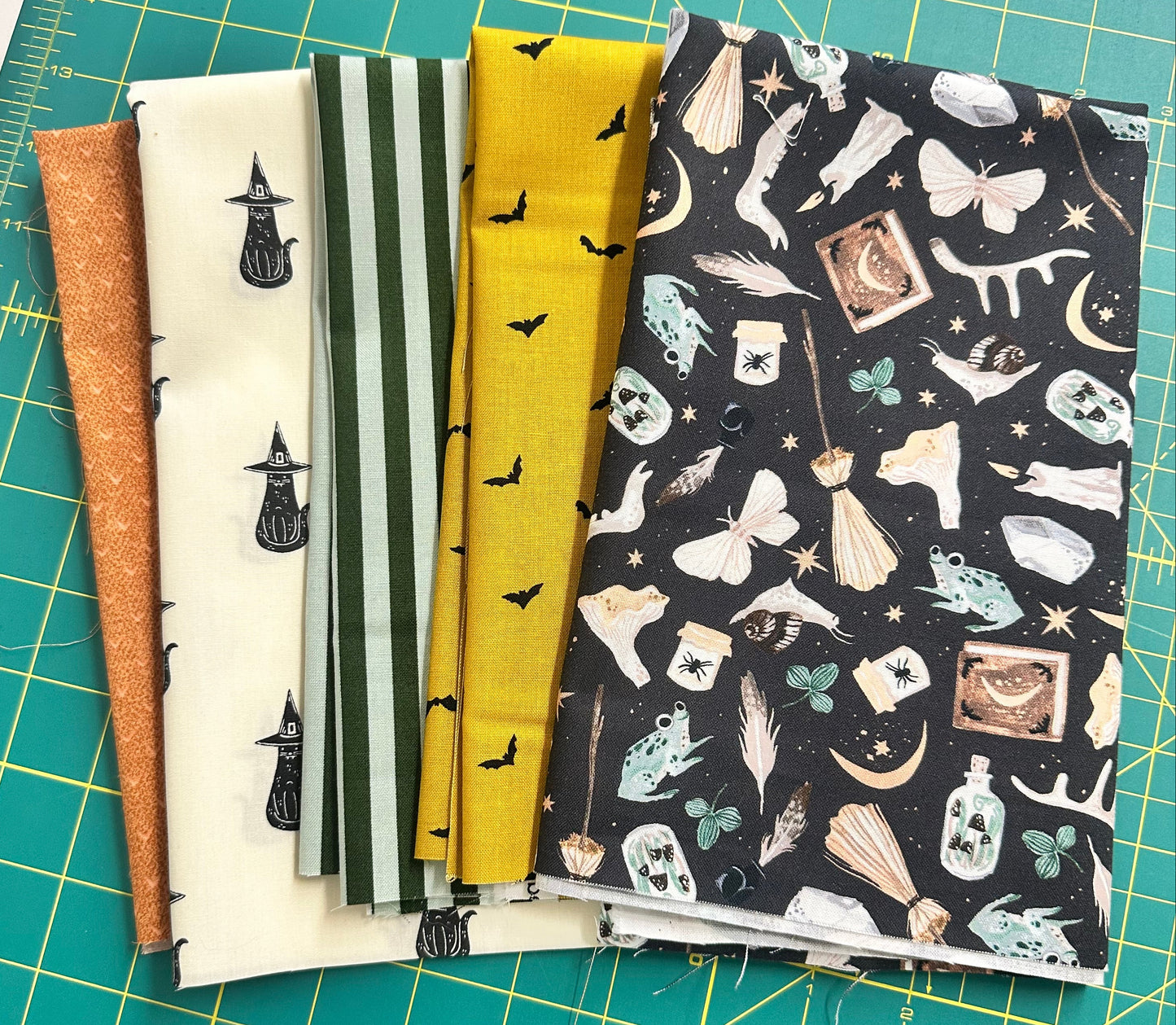 Stack of Halloween fabric samples with various patterns on a green cutting mat.